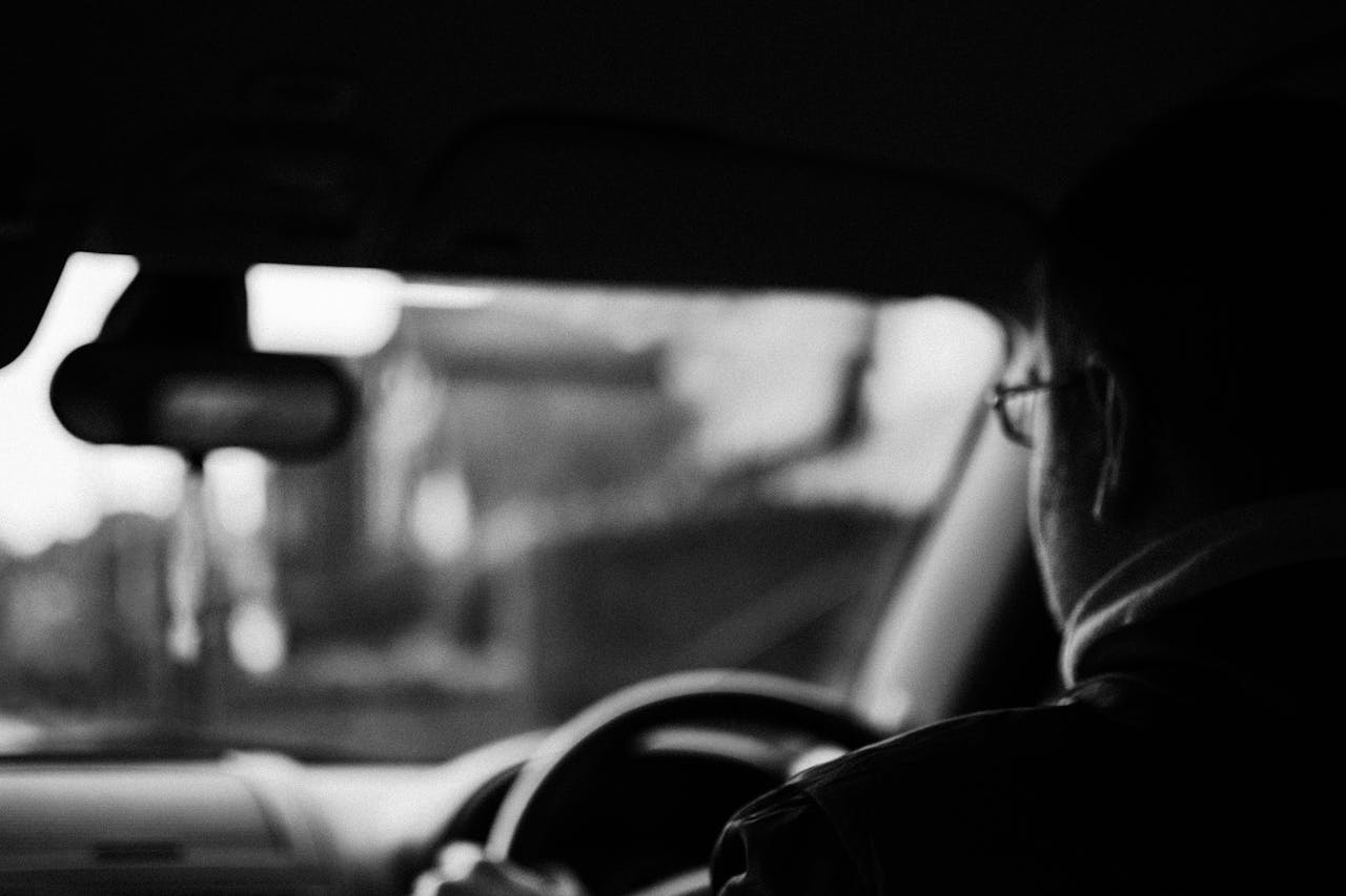 Moody backseat view of a man driving a car, emphasizing solitude and focus.